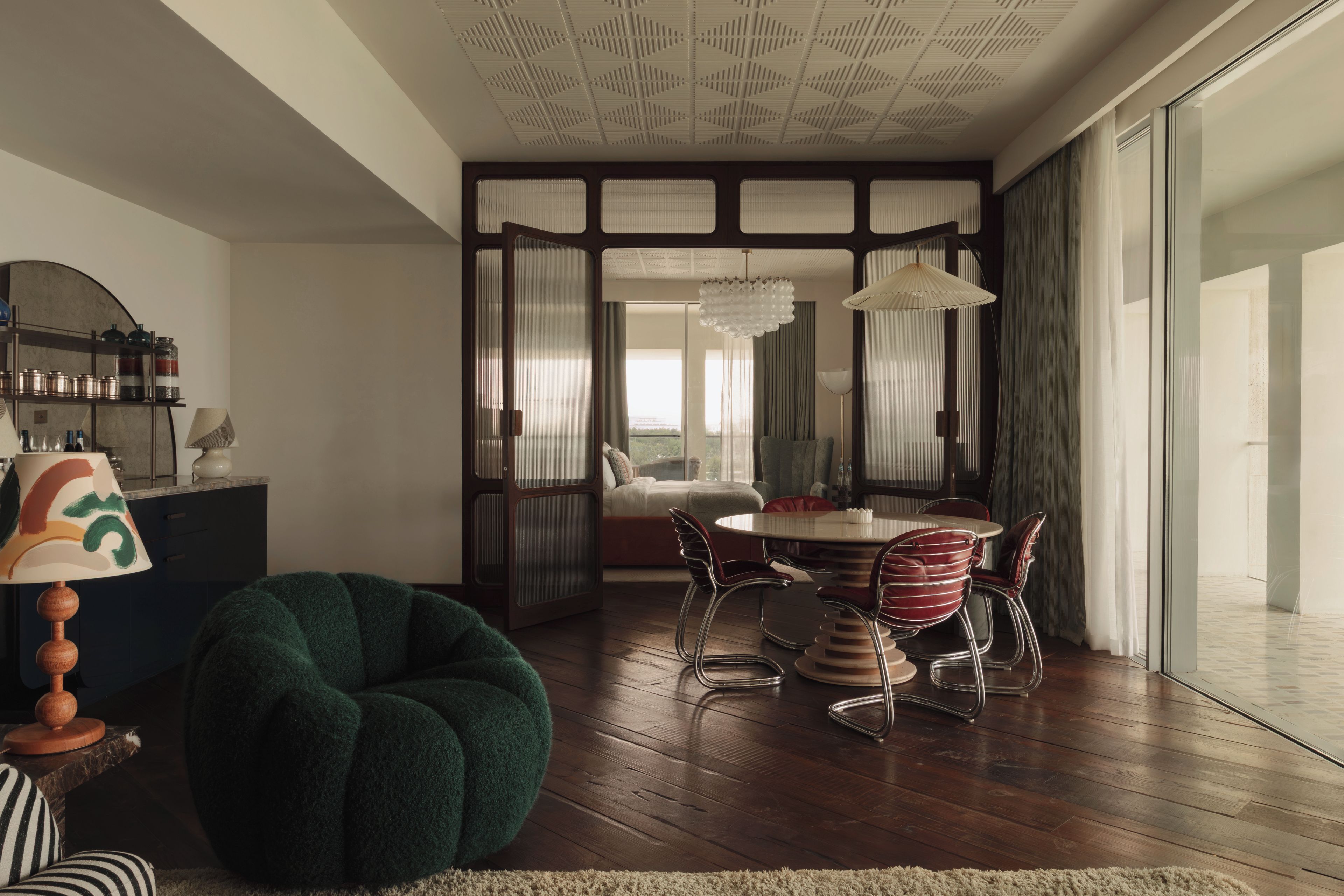 Ein modernes Wohnzimmer mit einem grünen Sessel, einem Essbereich mit rundem Tisch und Stühlen sowie einer Küchenzeile mit Schränken und einer Lampe.