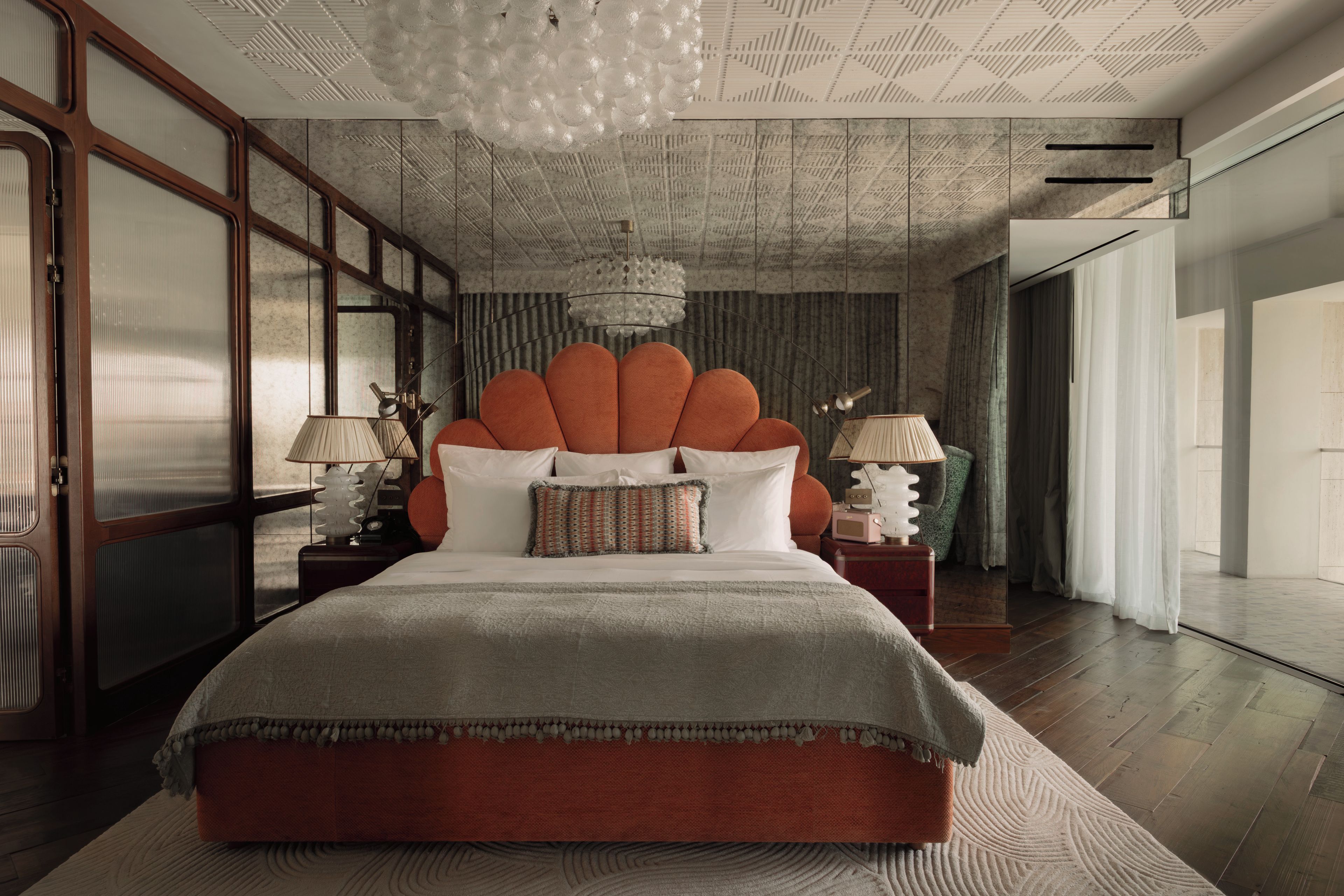 Ein Schlafzimmer mit einem großen Bett, zwei Nachttischen, einer Chandelüster und Blick ins Freie.