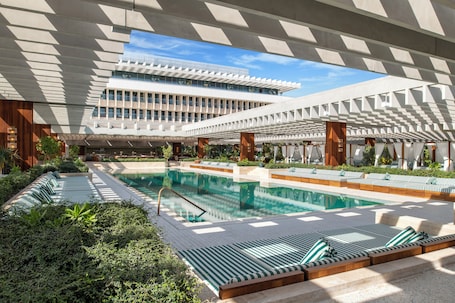 Una piscina al aire libre, sillones reclinables de piscina. The Ned Doha