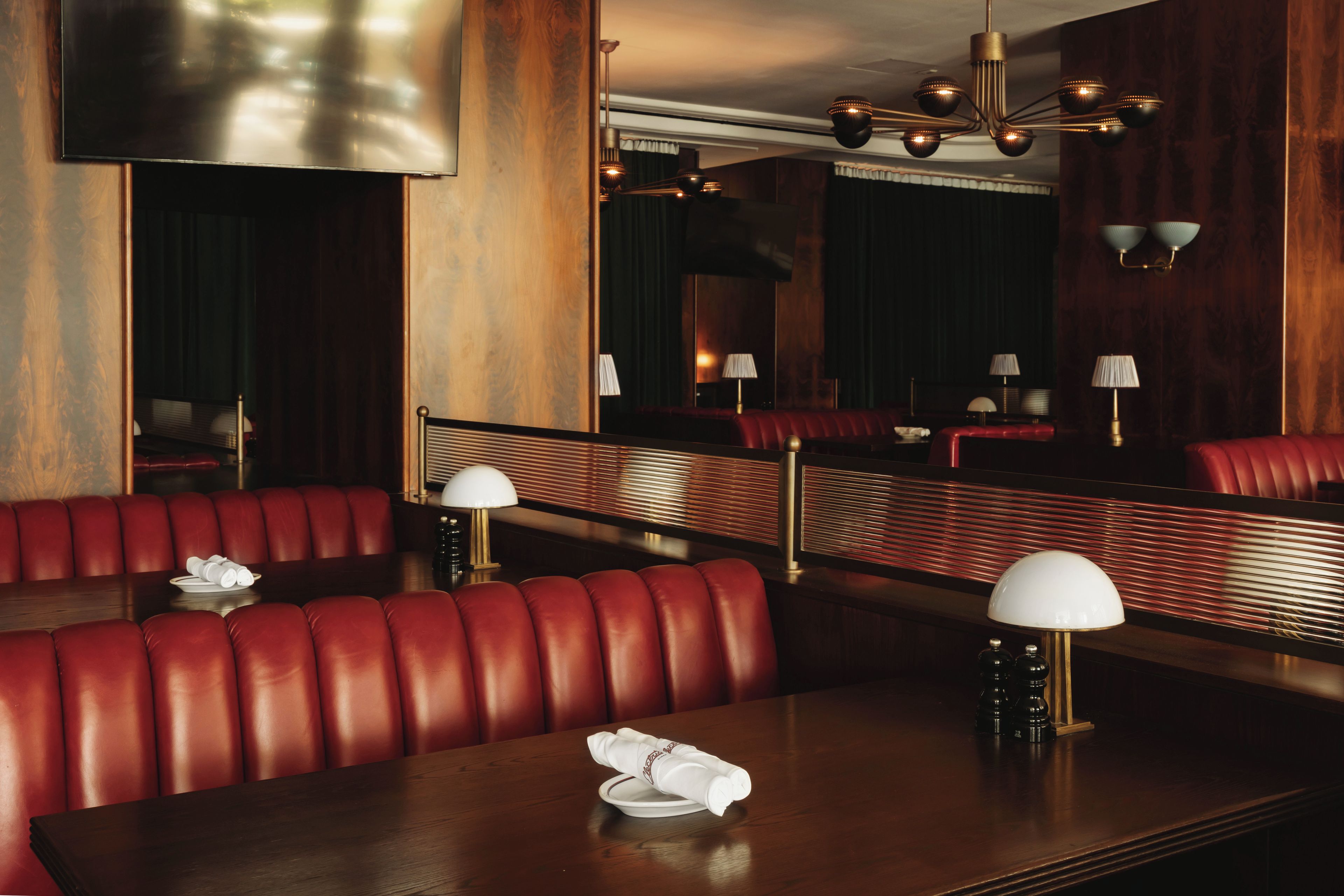 A restaurant with red leather booths, wooden tables, and modern lighting fixtures.