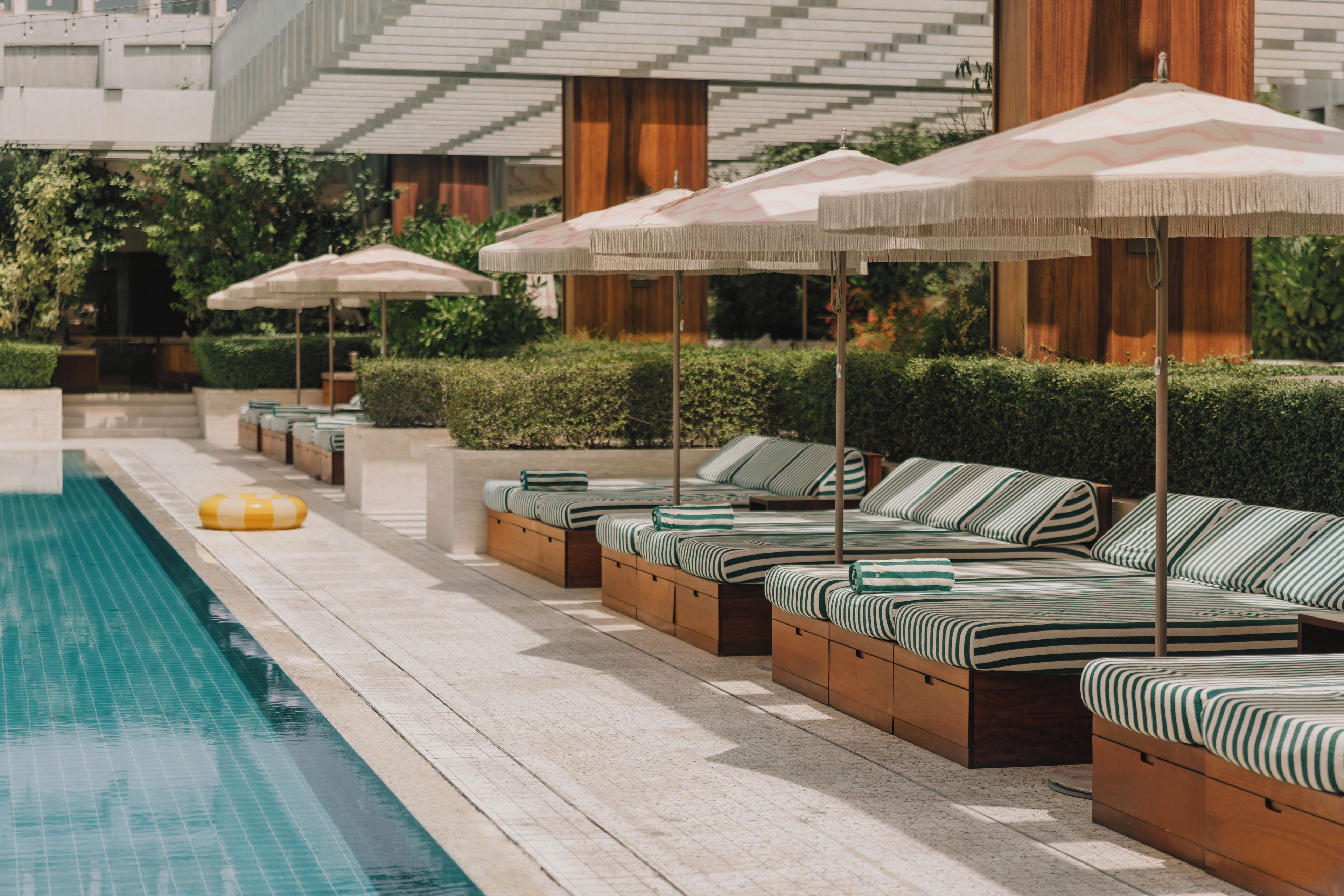 Zona junto a la piscina con sillones de descanso y sombrillas, una piscina y un edificio de diseño moderno.