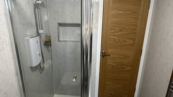 A glass-enclosed shower area with a control panel, a wooden door, and patterned floor tiles.