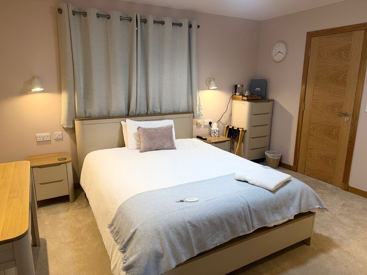 A neatly arranged bedroom with a bed, bedside tables, a nightstand, a clock, and a wardrobe.