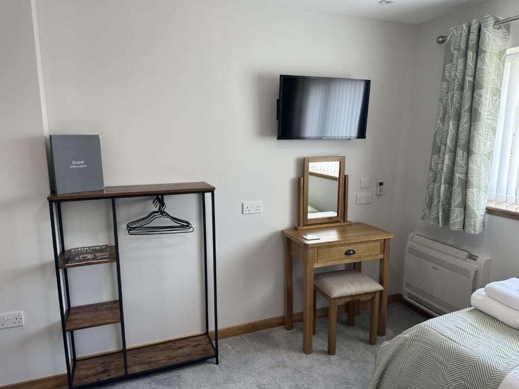 A bedroom with a wooden dresser, a mirror, a television mounted on the wall, and a window with curtains.