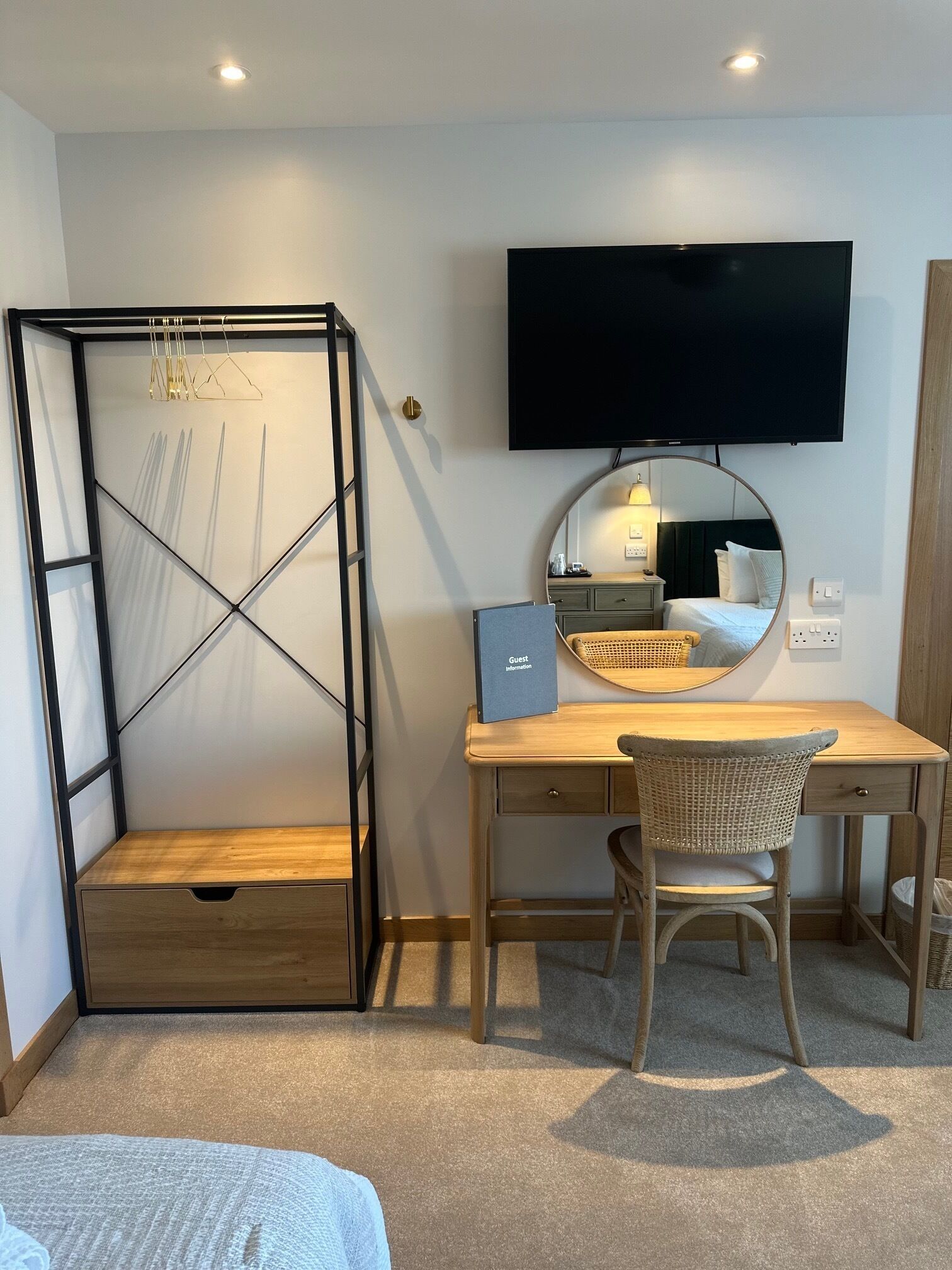 A hotel room with a bed, a desk with a chair, a TV, a mirror, and a hanging light fixture.