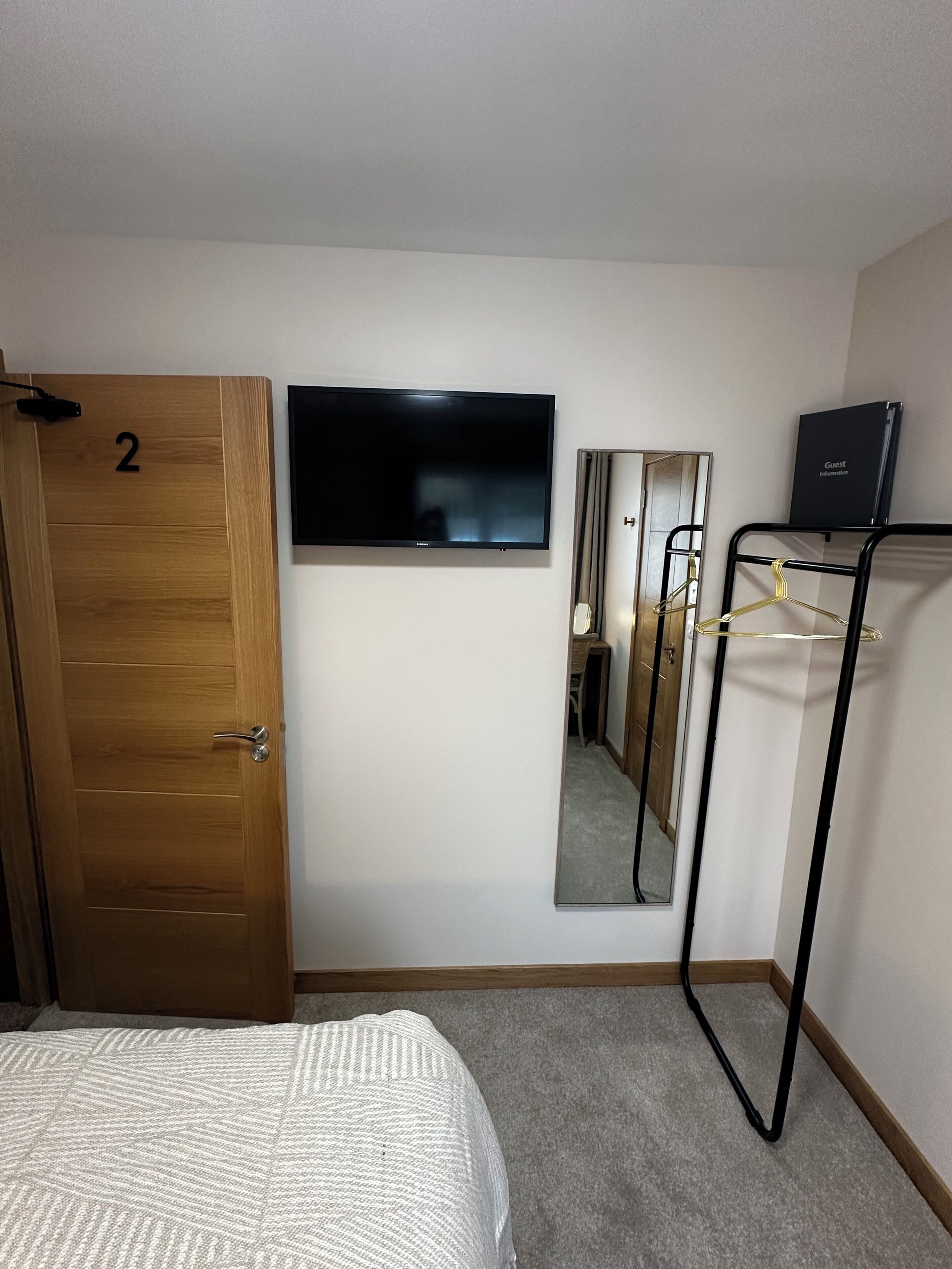 A hotel room with a bed, a television, a mirror, and a coat rack.