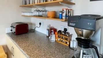 A kitchen with a coffee maker, shelves with jars, a toaster, and a wooden cabinet.