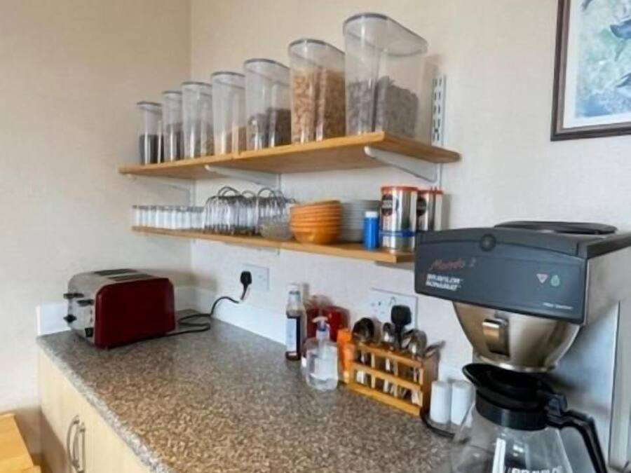 A kitchen with a coffee maker, shelves with jars, a toaster, and a wooden cabinet.