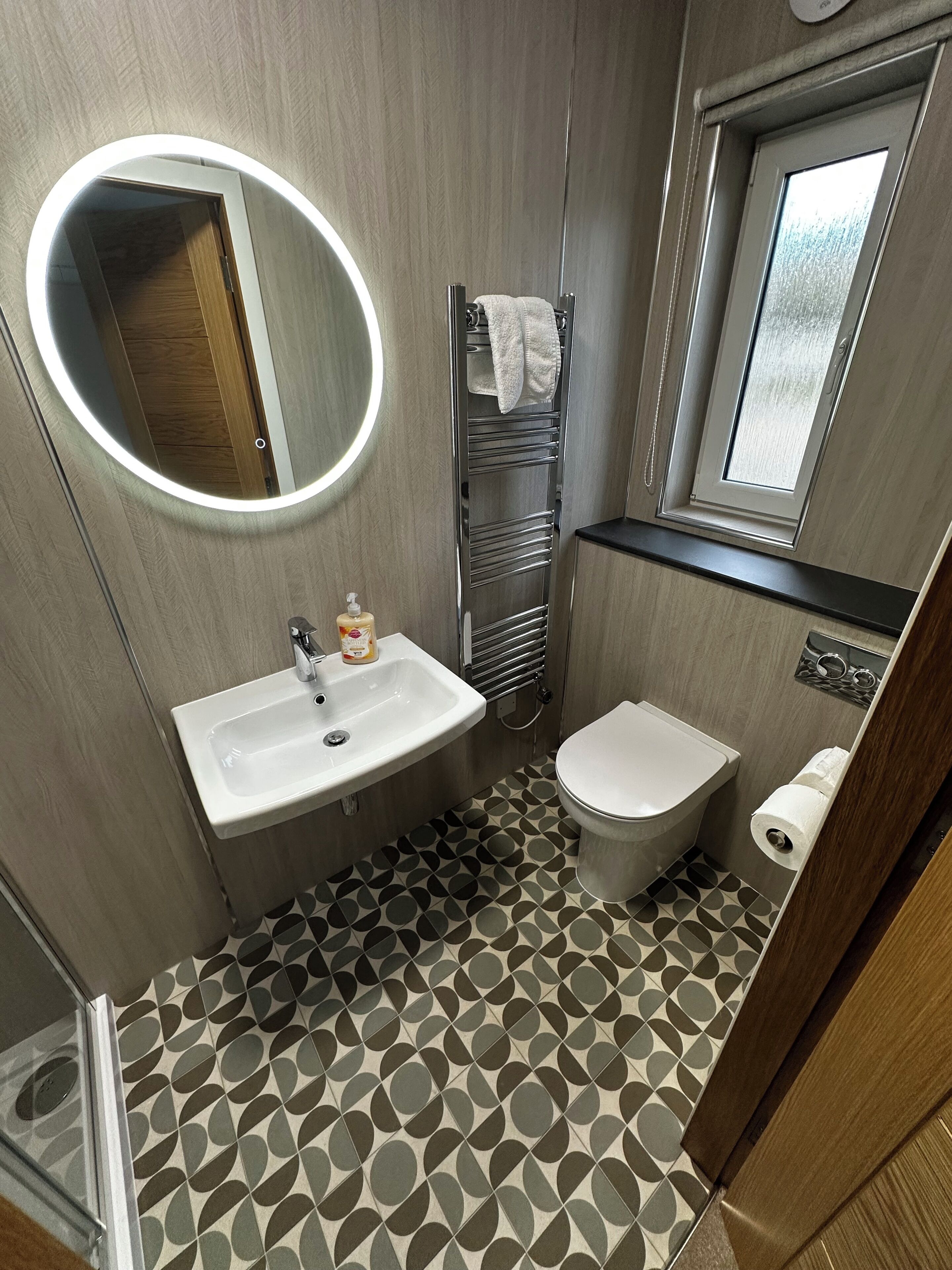 A compact bathroom with a round mirror, a sink, a toilet, and a towel rack.