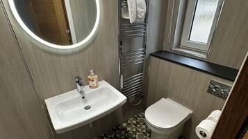 A compact bathroom with a round mirror, a sink, a toilet, and a towel rack.