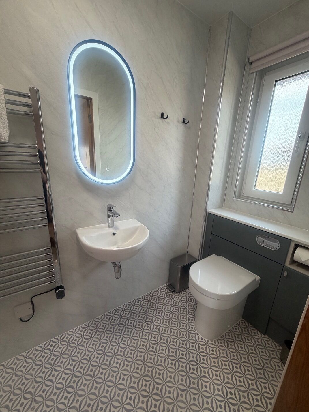 A bathroom with a white sink, a mirror with a light, a toilet, and a patterned floor.