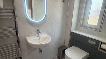 A bathroom with a white sink, a mirror with a light, a toilet, and a patterned floor.