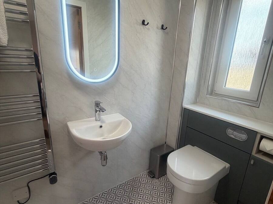 A bathroom with a white sink, a mirror with a light, a toilet, and a patterned floor.