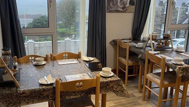 A dining area with wooden tables and chairs, large windows with curtains, and a view of the outside.