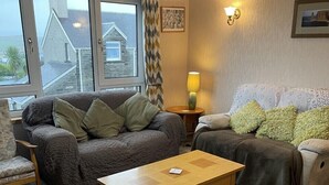 A cozy living room with two sofas, a wooden coffee table, and a view of a house through large windows.
