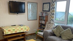 A living room with a wooden coffee table, a sofa, a bookshelf, and a flat-screen TV mounted on the wall.