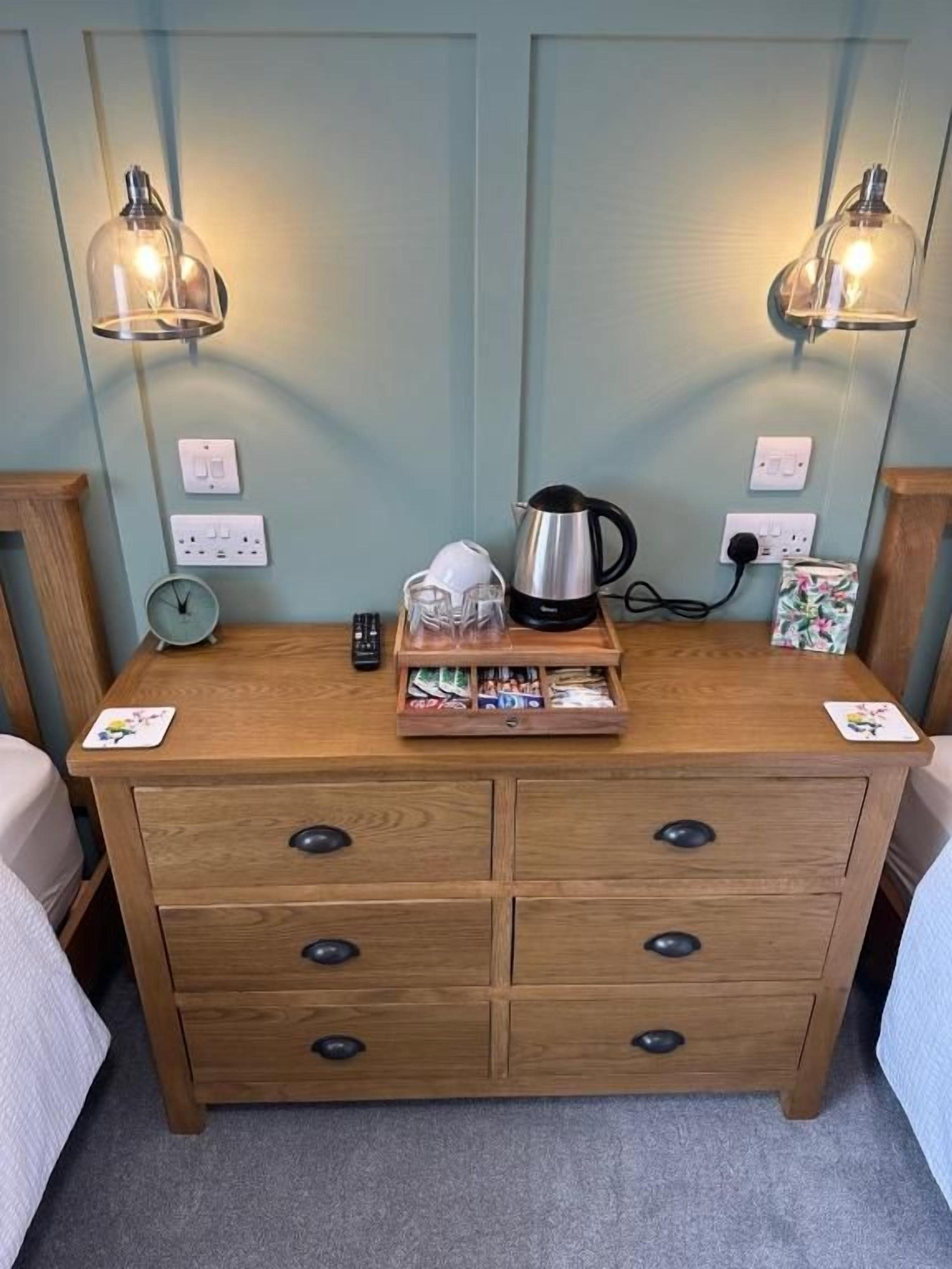 Une commode en bois avec des tiroirs, une bouilloire, une horloge et une lampe.