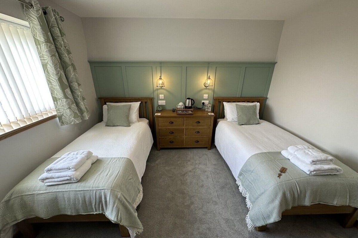 Ein Zweibettzimmer mit zwei Einzelbetten, einem Nachttisch aus Holz und einem Spiegel.