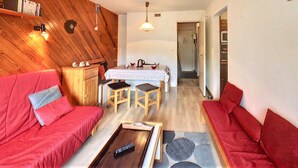 Ein gemütliches Wohnzimmer mit einem roten Sofa, einem Holzesstisch mit zwei Stühlen und einer Küchenzeile im Hintergrund.