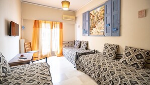 Une chambre avec deux lits, un bureau et une chaise. Elle est équipée d’une fenêtre avec des rideaux, d’un climatiseur et d’un téléviseur fixé au mur.