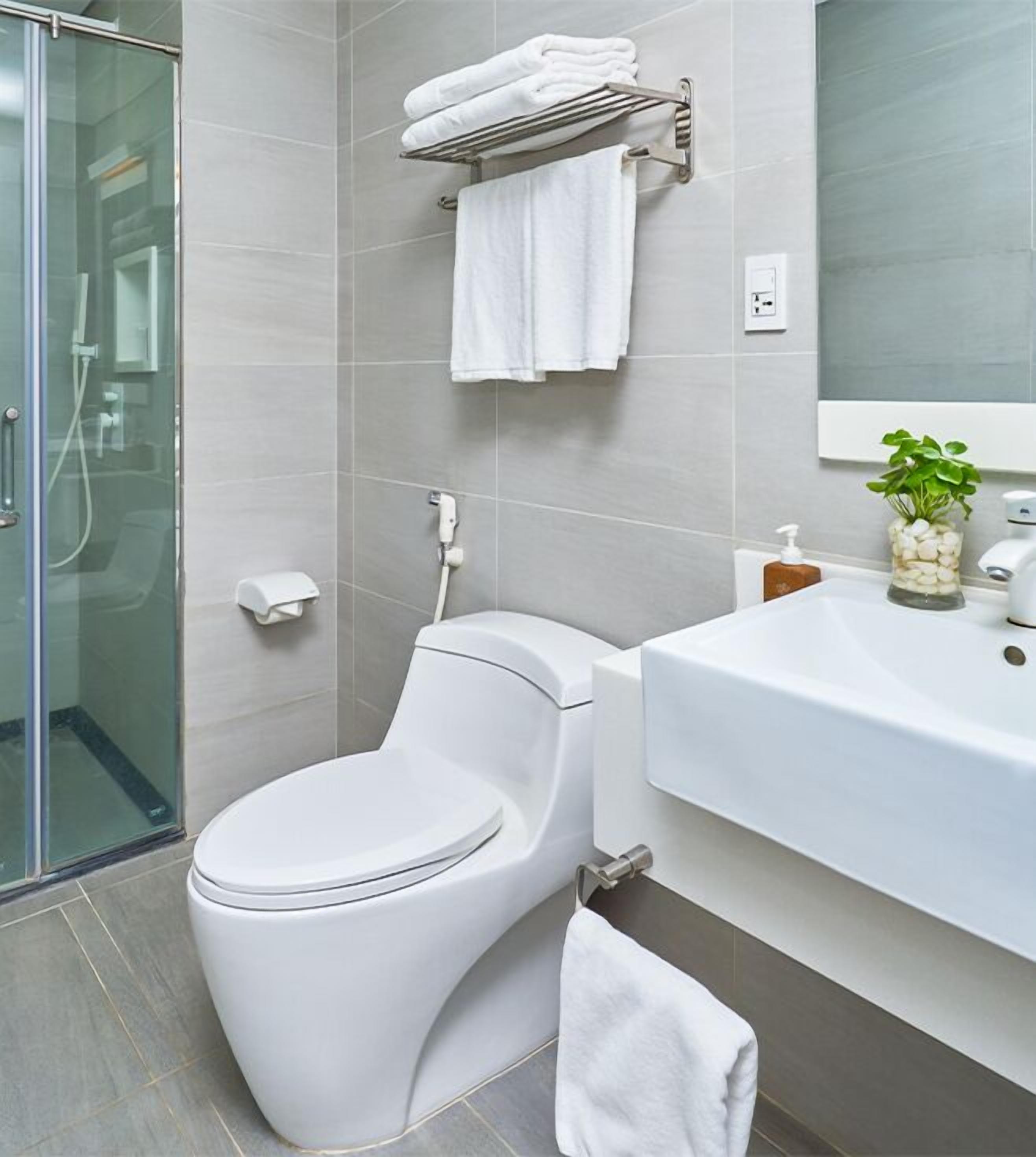 A modern bathroom with a toilet, a glass shower enclosure, a sink with a plant, and a towel rack.