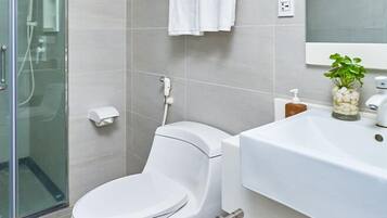 A modern bathroom with a toilet, a glass shower enclosure, a sink with a plant, and a towel rack.