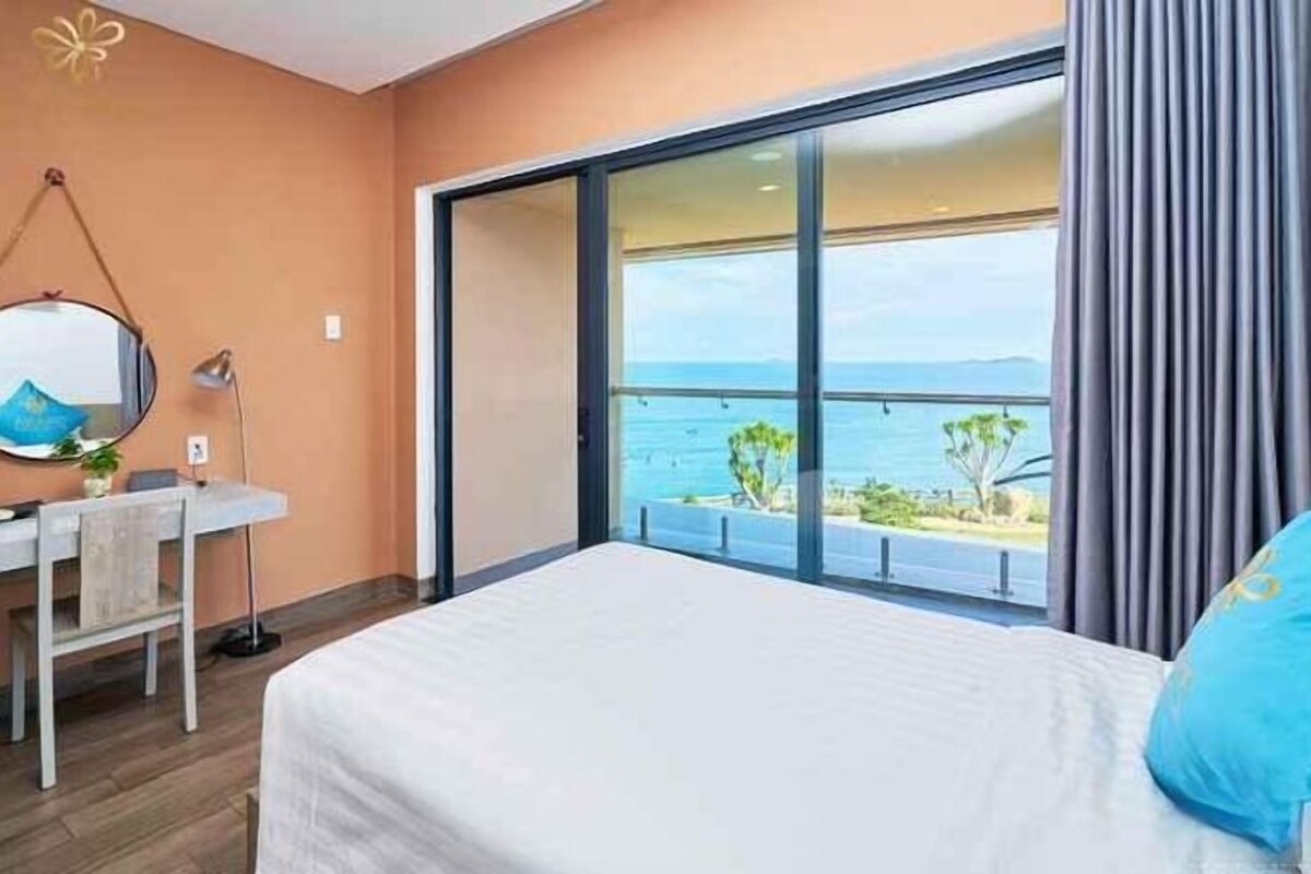 A hotel room with a bed, a desk, and a view of the sea.