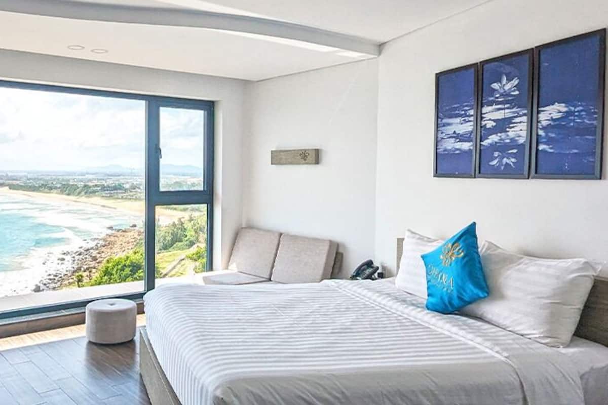 Une chambre avec une grande fenêtre donnant sur la plage et l’océan.