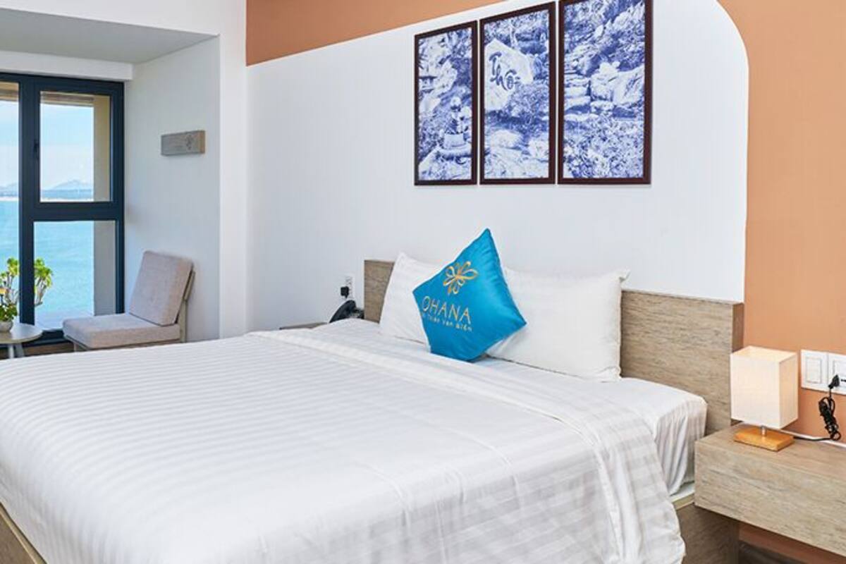 Une chambre d’hôtel avec un grand lit, une chaise, une petite table et une vue sur la mer.