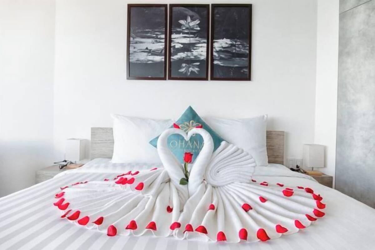 Un lit avec un oreiller en forme de cygne et une couvre-lit également en forme de cygne, un mur orné de trois tableaux encadrés et une table de chevet avec une lampe.