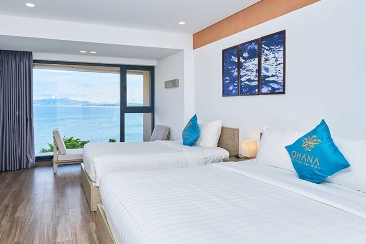 Une chambre d’hôtel avec deux lits, un bureau et une grande fenêtre donnant sur la mer.