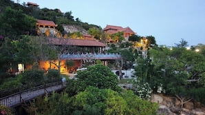 A traditional-style building with a red roof, surrounded by lush greenery and a stone pathway. - Ohana Village (Cat Tien)