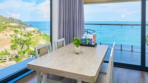 A balcony with a wooden table and chairs, a potted plant, and a beverage tray. - Ohana Village (Cat Tien)