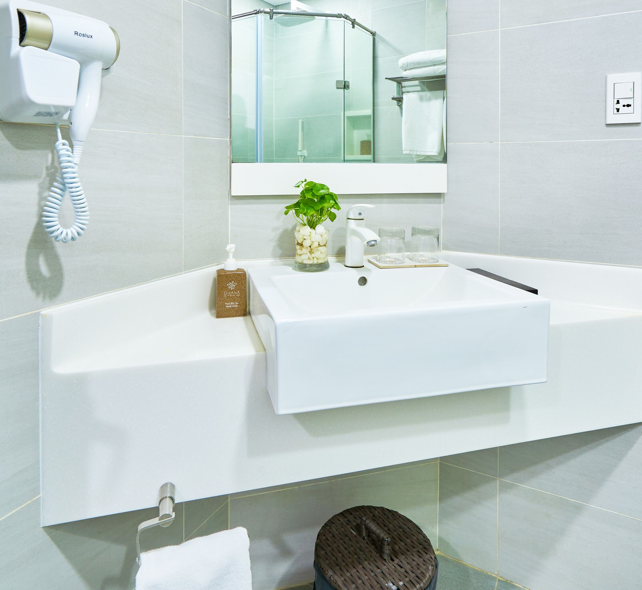 Ein modernes Badezimmer mit einem weißen Waschbecken, einem Handtrockner, einer Pflanze und einem Spiegel über dem Waschbecken.