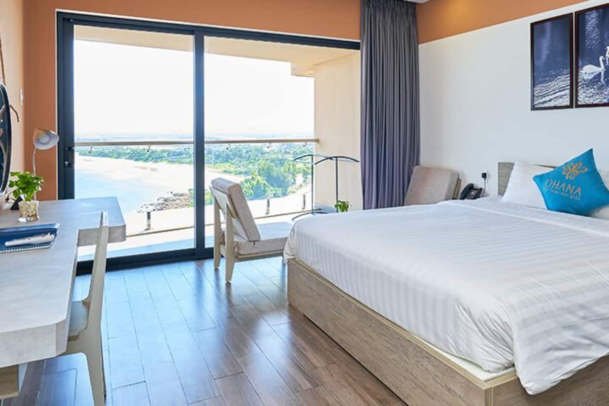 Une chambre d’hôtel avec un grand lit, un bureau avec une chaise, un balcon avec vue et un tableau au mur.