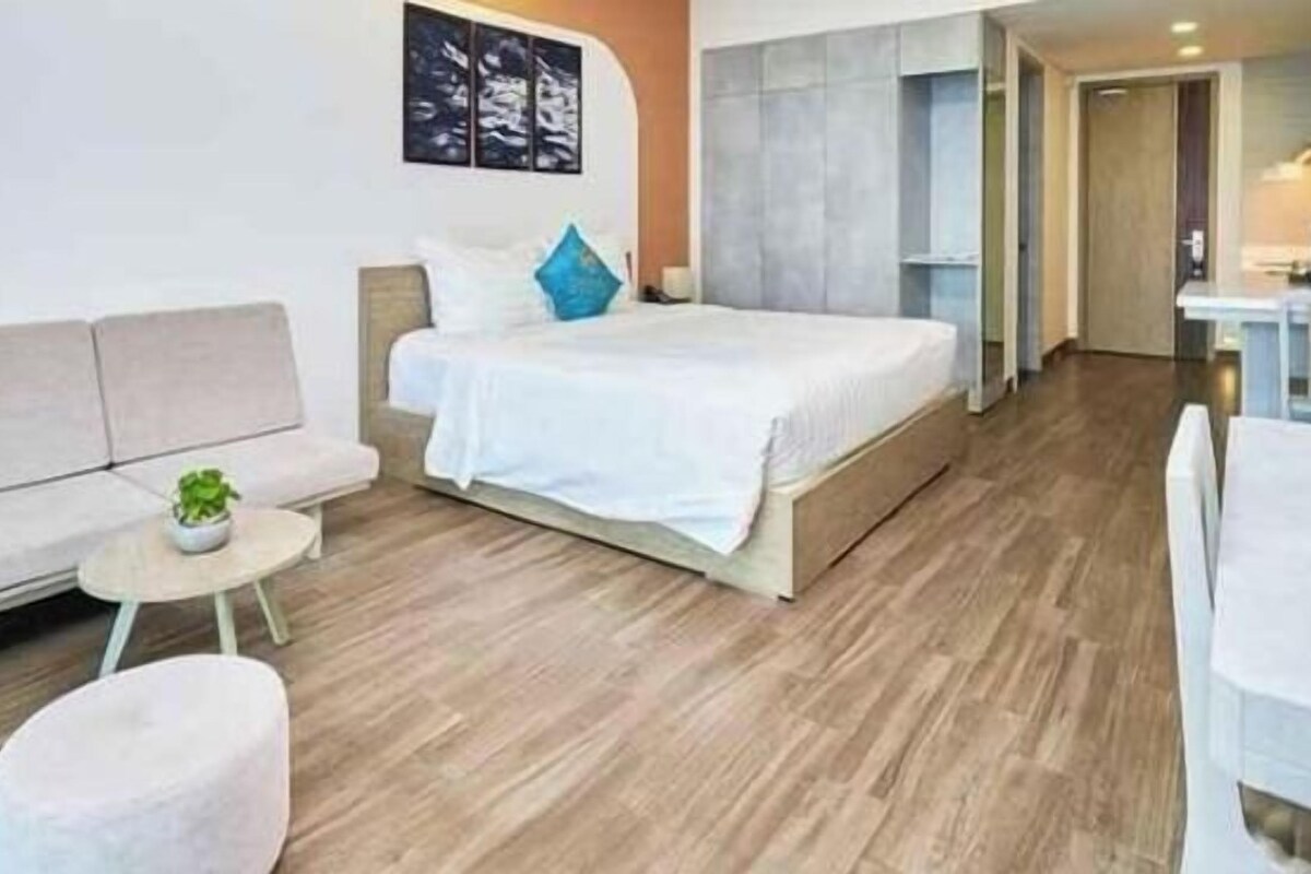 A modern hotel room with a bed, sofa, and a small table with a plant.