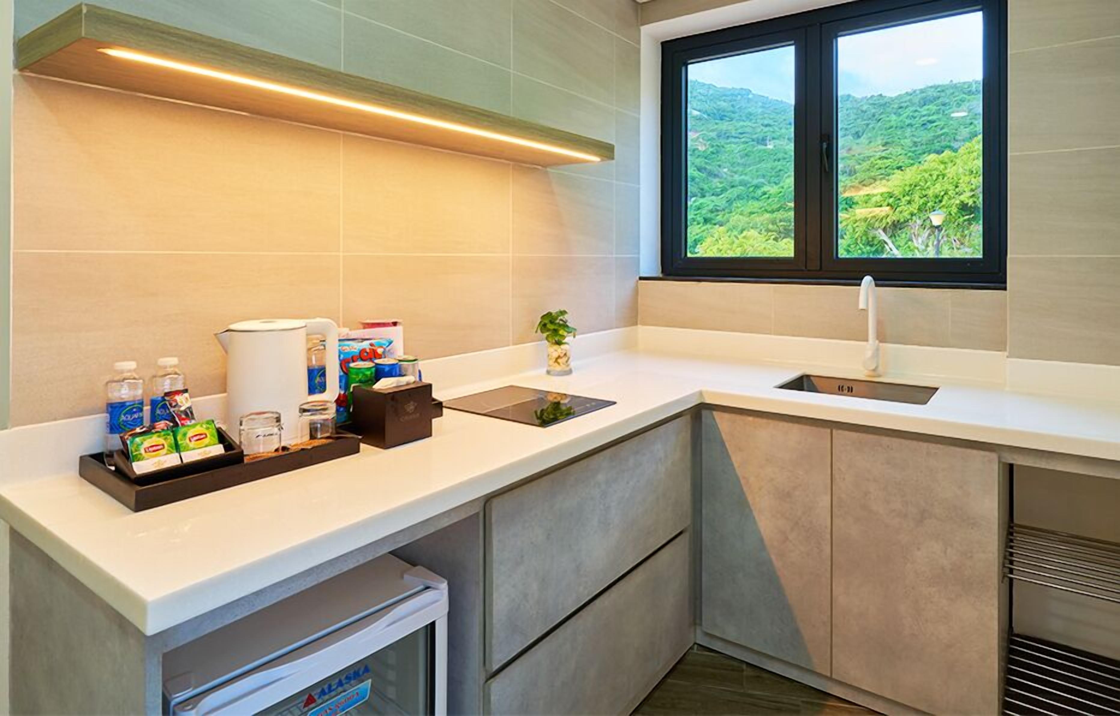 A modern kitchen with a built-in sink, a window with a view of greenery, and a countertop with various items.