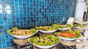 A buffet with various salads and vegetables displayed on wooden stands. - Ohana Village (Cat Tien)