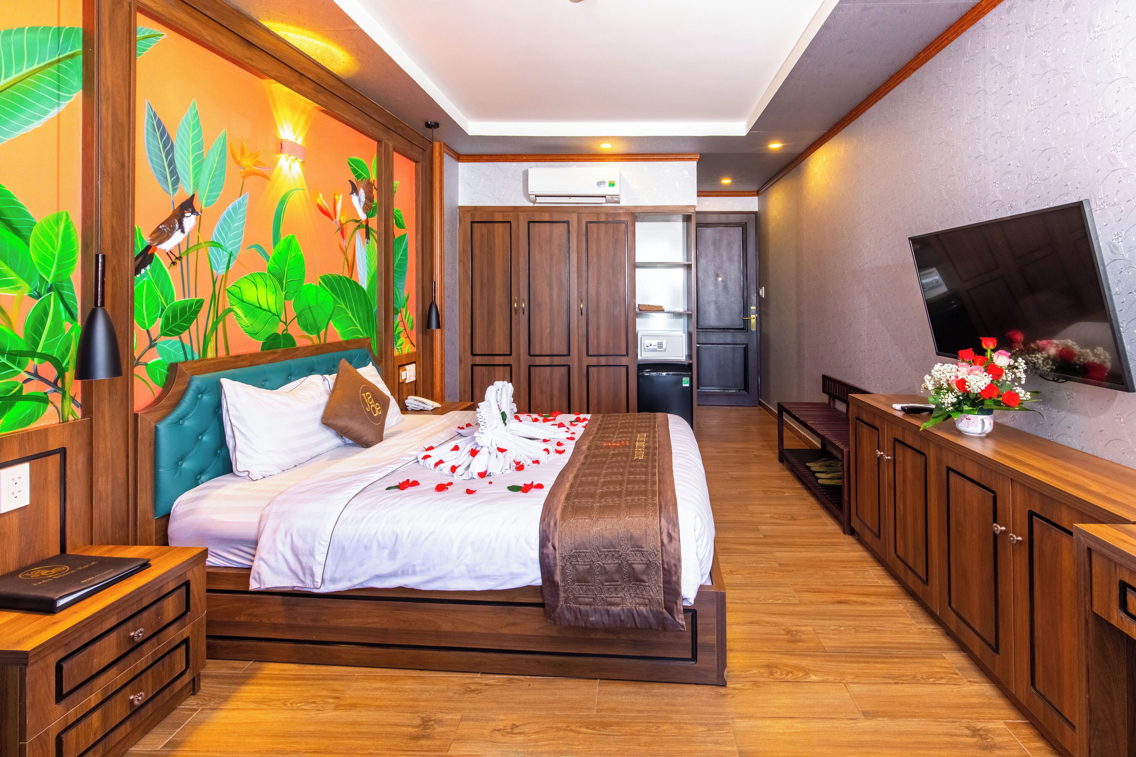 A bedroom with a bed, wooden cabinets, a television, and a wall with a nature-themed mural.
