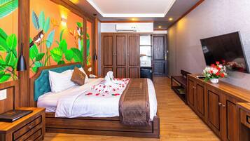A bedroom with a bed, wooden cabinets, a television, and a wall with a nature-themed mural.