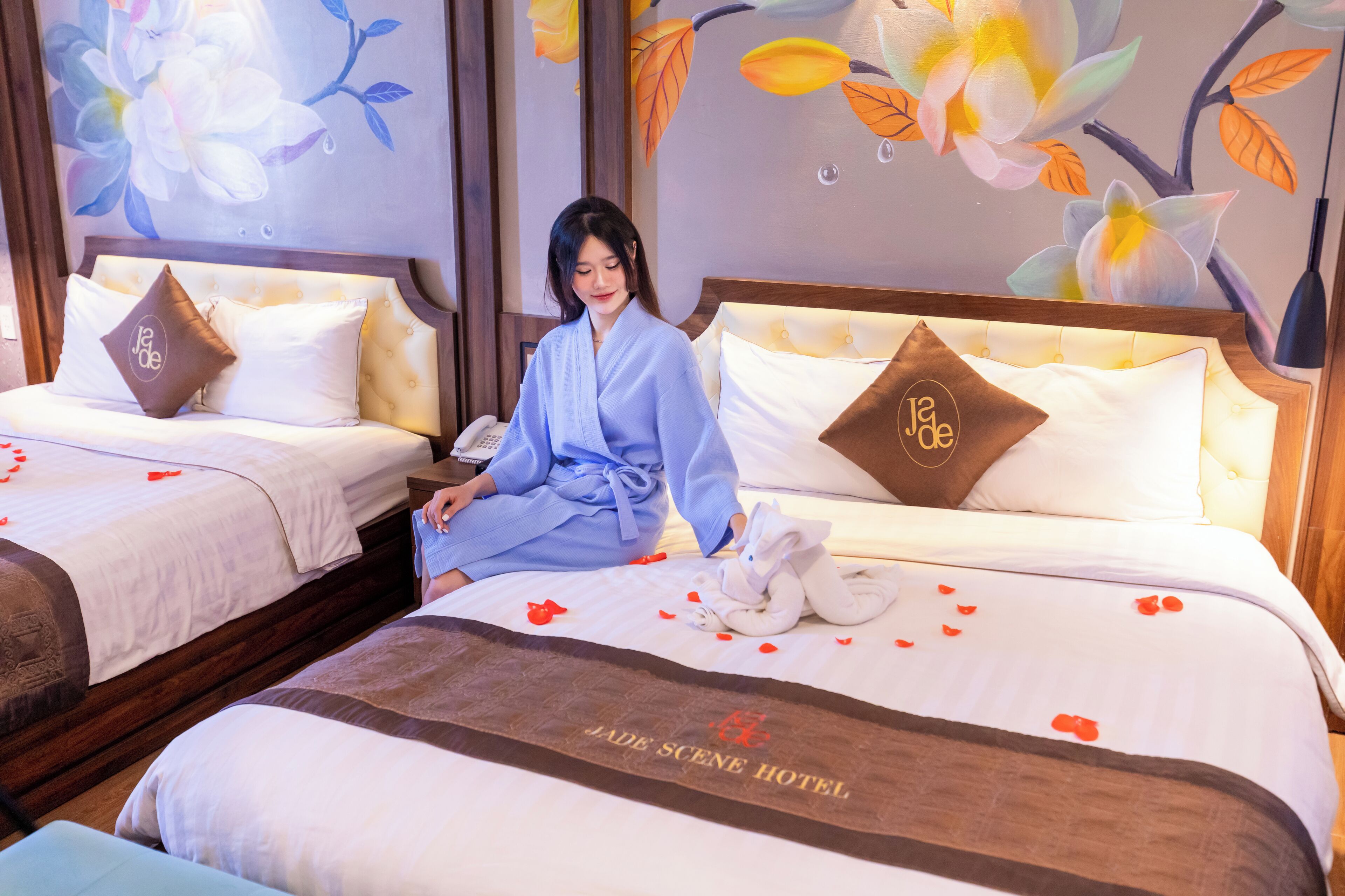 Habitación de hotel con dos camas, cada una con un corredor de cama del 'Jade Scene Hotel', una bata suave y una toalla blanca con un conejo.