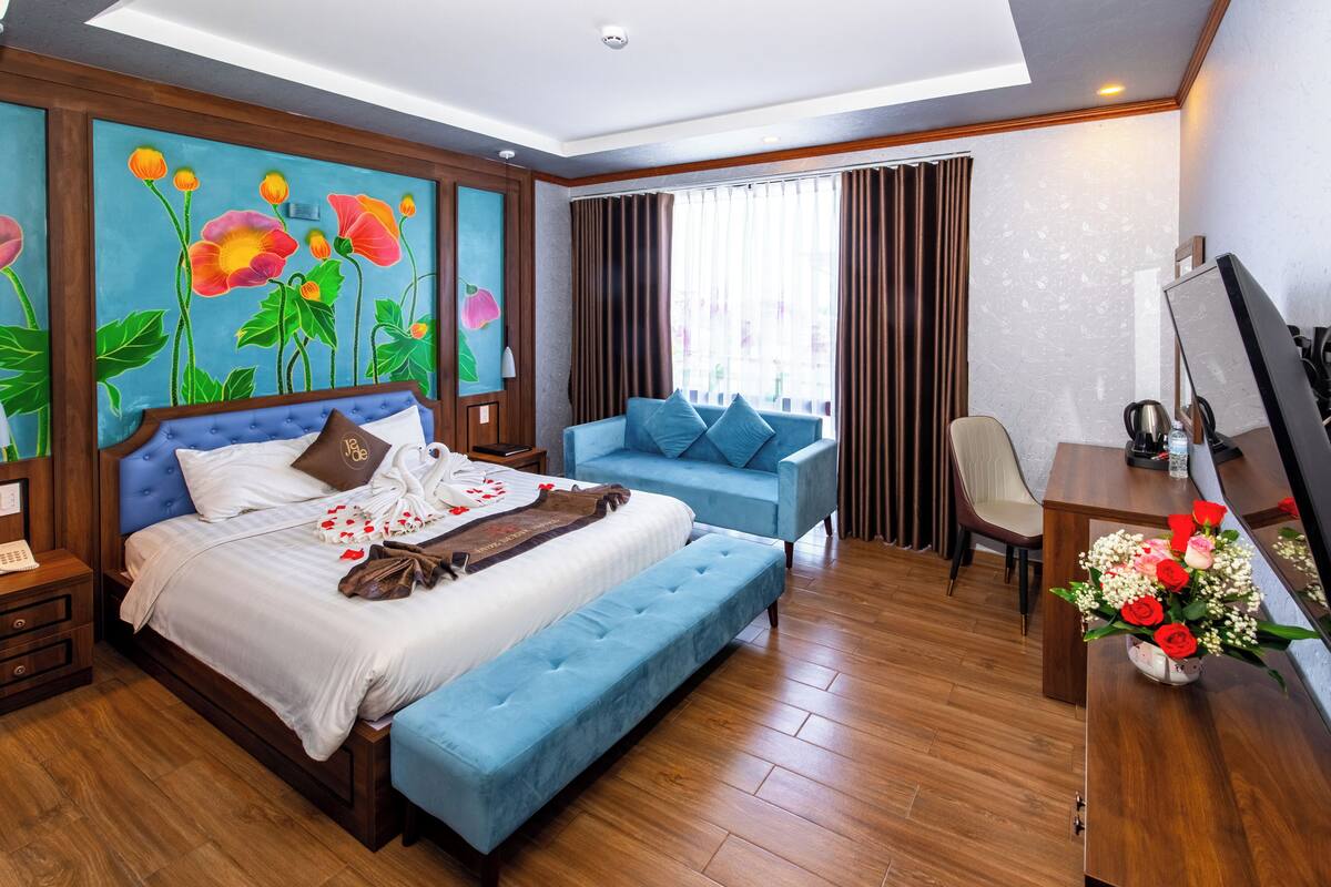A hotel room with a large bed, a sofa, a desk, and a TV.