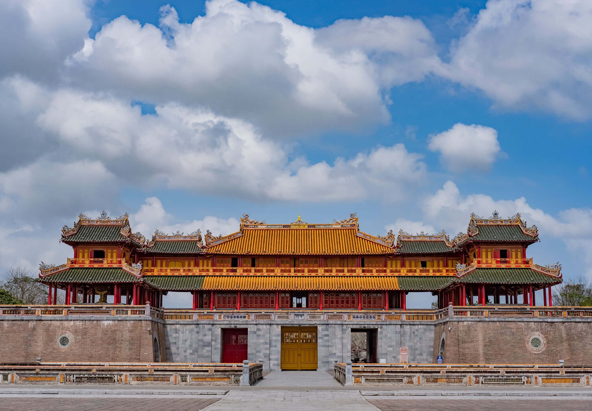 A traditional multi-tiered building with a prominent central entrance, surrounded by a low wall and a paved area.