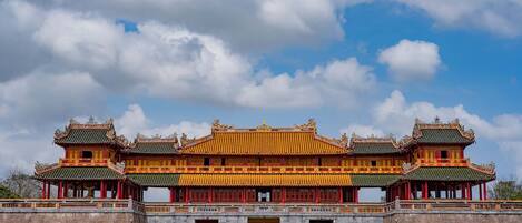 A traditional multi-tiered building with a prominent central entrance, surrounded by a low wall and a paved area.