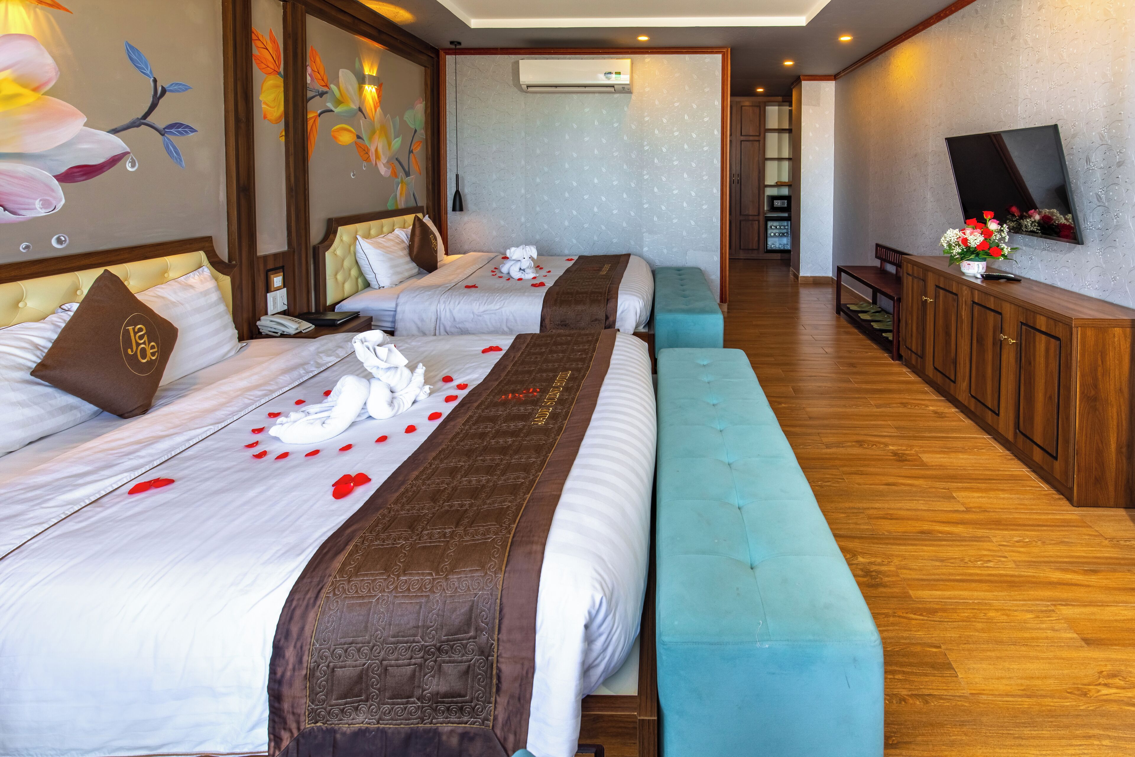 A hotel room with two beds, a bench, a TV, and a wooden cabinet.