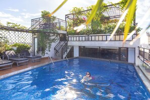 A swimming pool with a person swimming, surrounded by lounge chairs and a covered area with stairs. - Jade Scene Hotel (Hue)