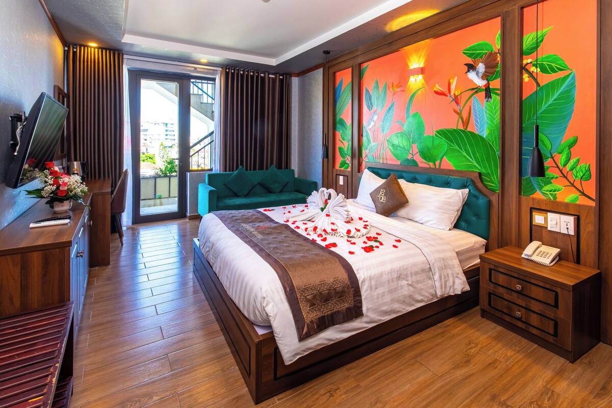 A hotel room with a large bed, a desk with a computer, a TV, and a view of the city through the window.