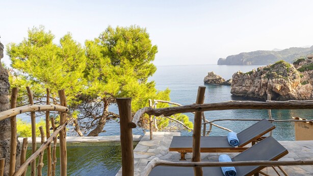 Terraza de piedra con dos tumbonas y una pérgola de madera con vistas al mar.