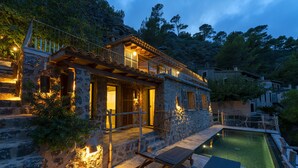 Una casa de piedra con piscina, terraza de madera y mobiliario exterior.