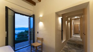 Pasillo con suelo de piedra, una silla y vista a un lago a través de una puerta abierta.